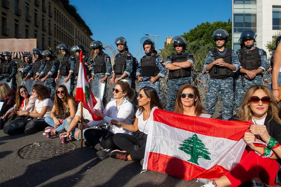 Women holding Lebanese flag sit in front of a line of soldiers